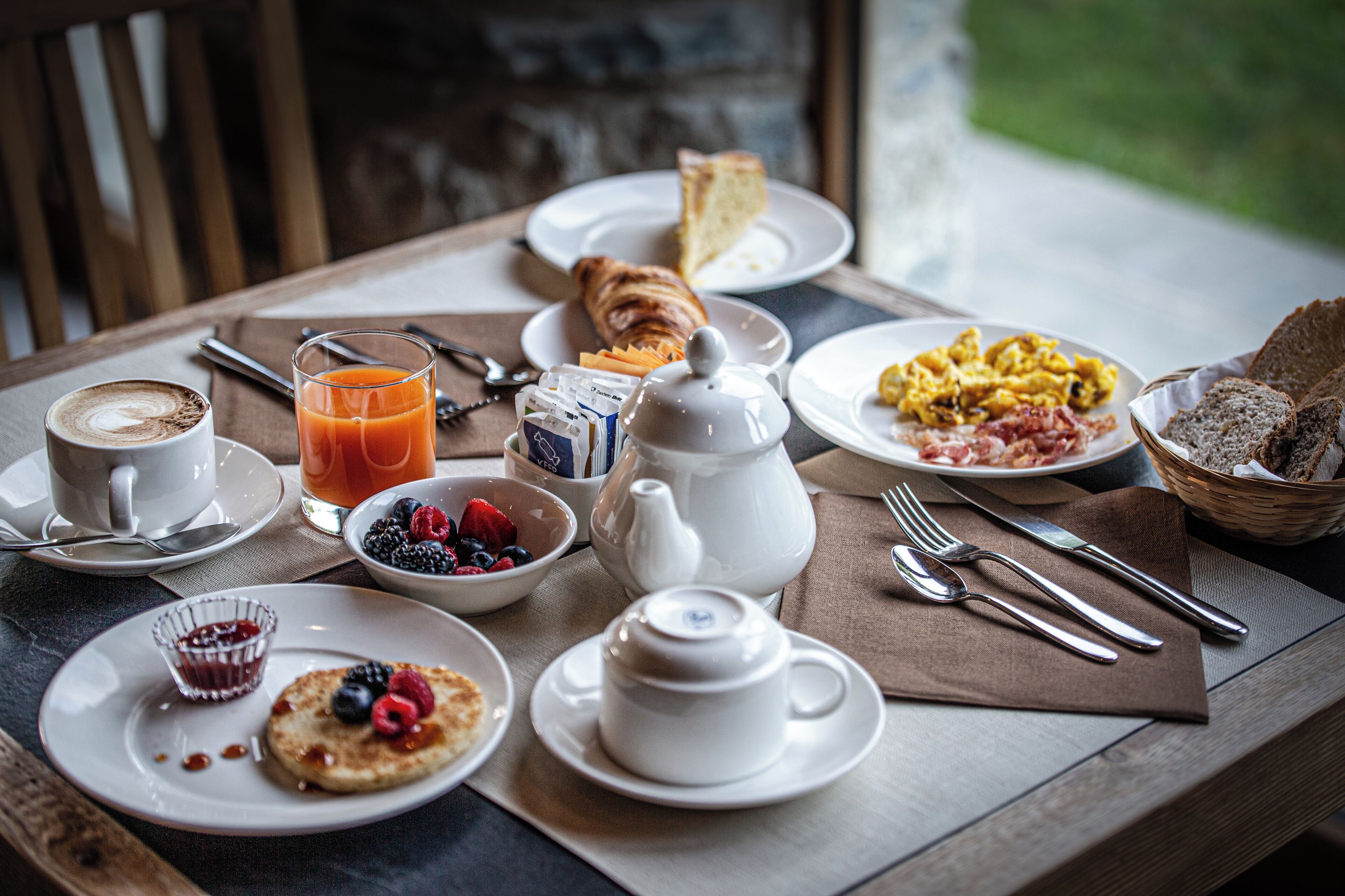 Une table de petit-déjeuner avec des assiettes remplies de nourriture, une théière, des tasses et des couverts.