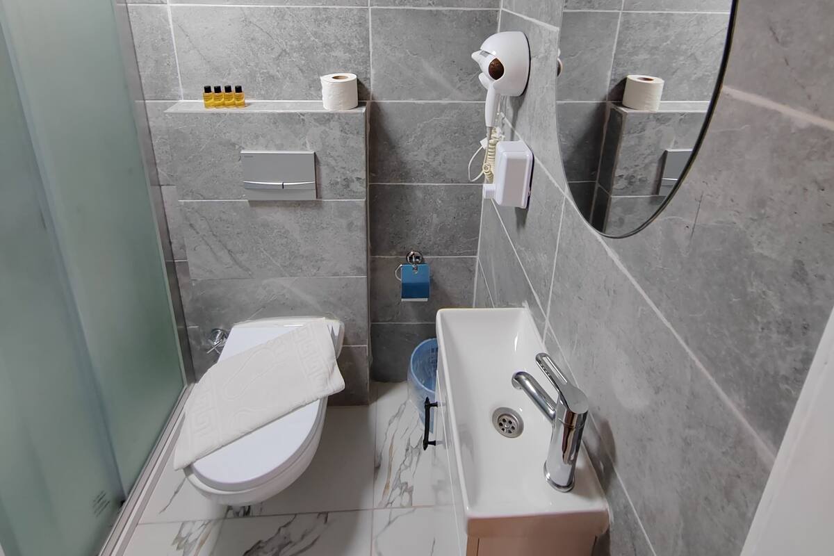 Baño con inodoro, lavamanos, espejo y dispensador de toallas.