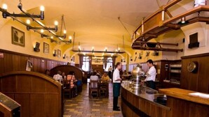 A restaurant interior with wooden booths, a central bar, and a tiled floor. - U Medvidku (Prague)