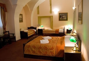 A hotel room with two beds, a desk, and a chair. There are lamps on the nightstands and a painting on the wall.