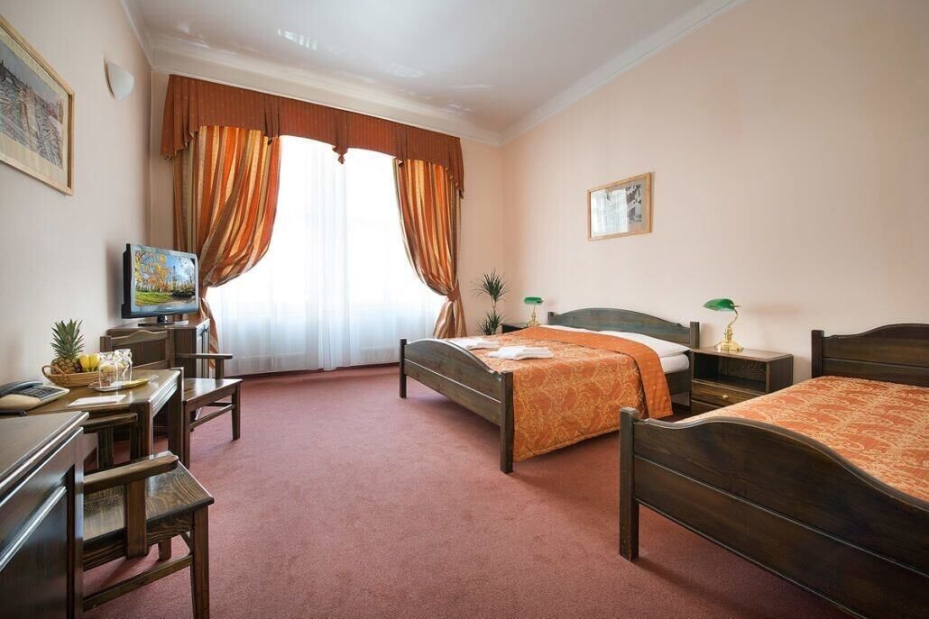 A hotel room with two beds, a desk, a television, and a window with curtains.