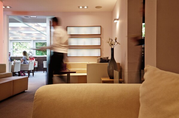 Un moderno vestíbulo de hotel con un área de estar, una recepción y un amplio ventanal que proporciona luz natural.