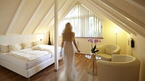A bedroom with a bed, a chair, a small table with flowers, and a window with blinds. - Hotel Bonjour (Bad Soden am Taunus)