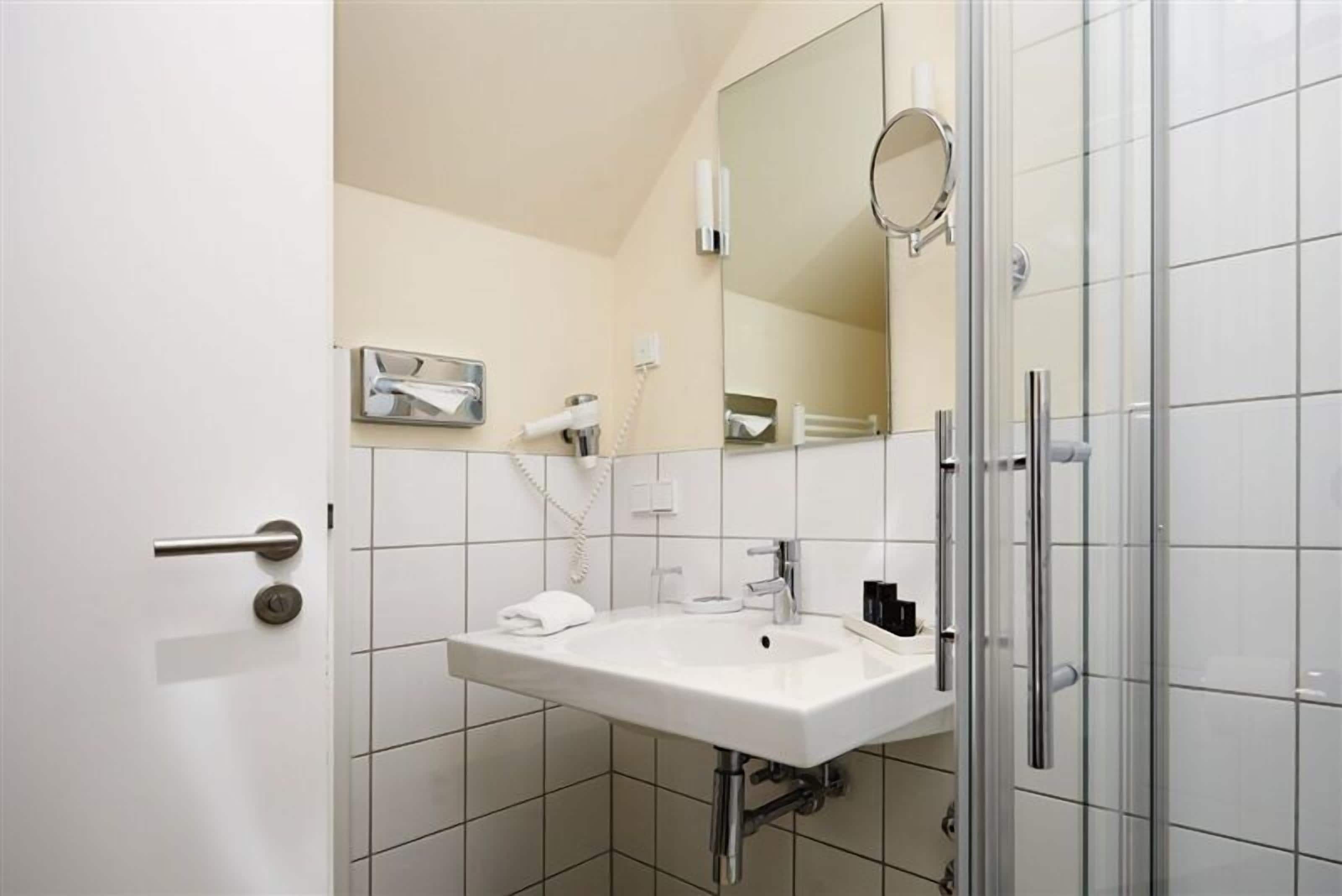 A modern bathroom with a white sink, a mirror, and a shower area.