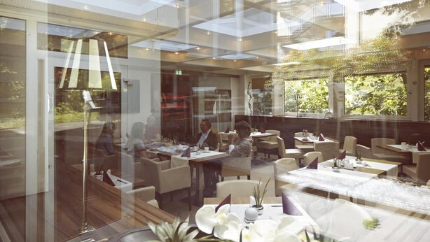 An indoor dining area with tables and chairs, large windows, and a modern ceiling design. - Hotel Bonjour (Bad Soden am Taunus)