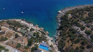 An aerial view of a coastal property with a swimming pool, lounge areas, and a rocky shoreline. - Kulube Hotel (Kas)