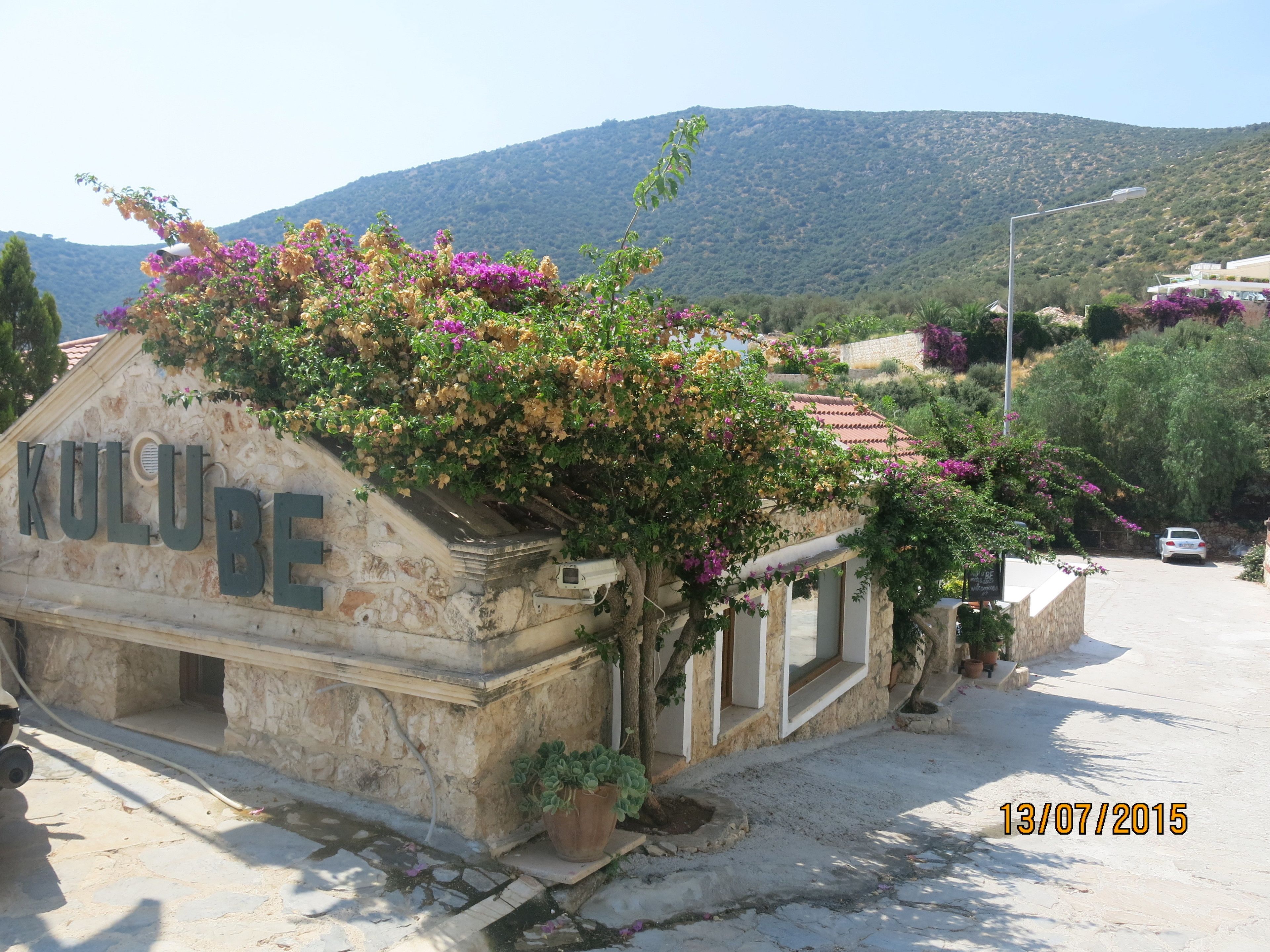 A stone building with a sign reading "KULUBE" and a mountain in the background.