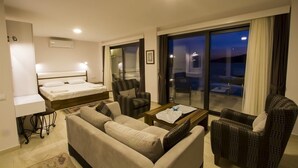 A hotel room with a bed, a sofa, a chair, a coffee table, and a balcony with a view. - Kulube Hotel (Kas)