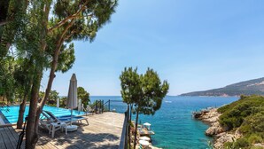 A wooden deck with lounge chairs and a pool, overlooking a clear blue sea and rocky coastline. - Kulube Hotel (Kas)