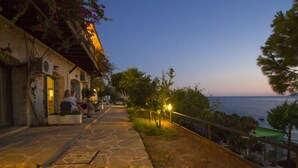 A stone pathway leading to a building with outdoor seating, overlooking a body of water. - Kulube Hotel (Kas)