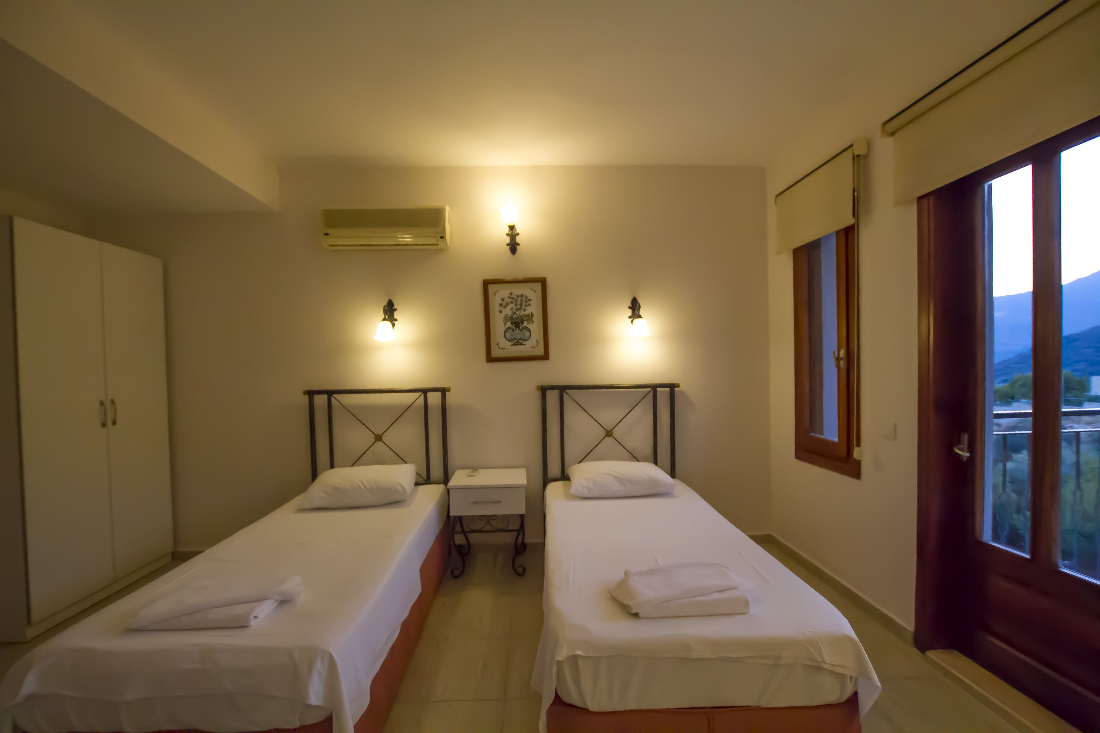A hotel room with two single beds, a wardrobe, a small table, and a window with a view.