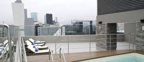A rooftop pool with lounge chairs and a cityscape view.