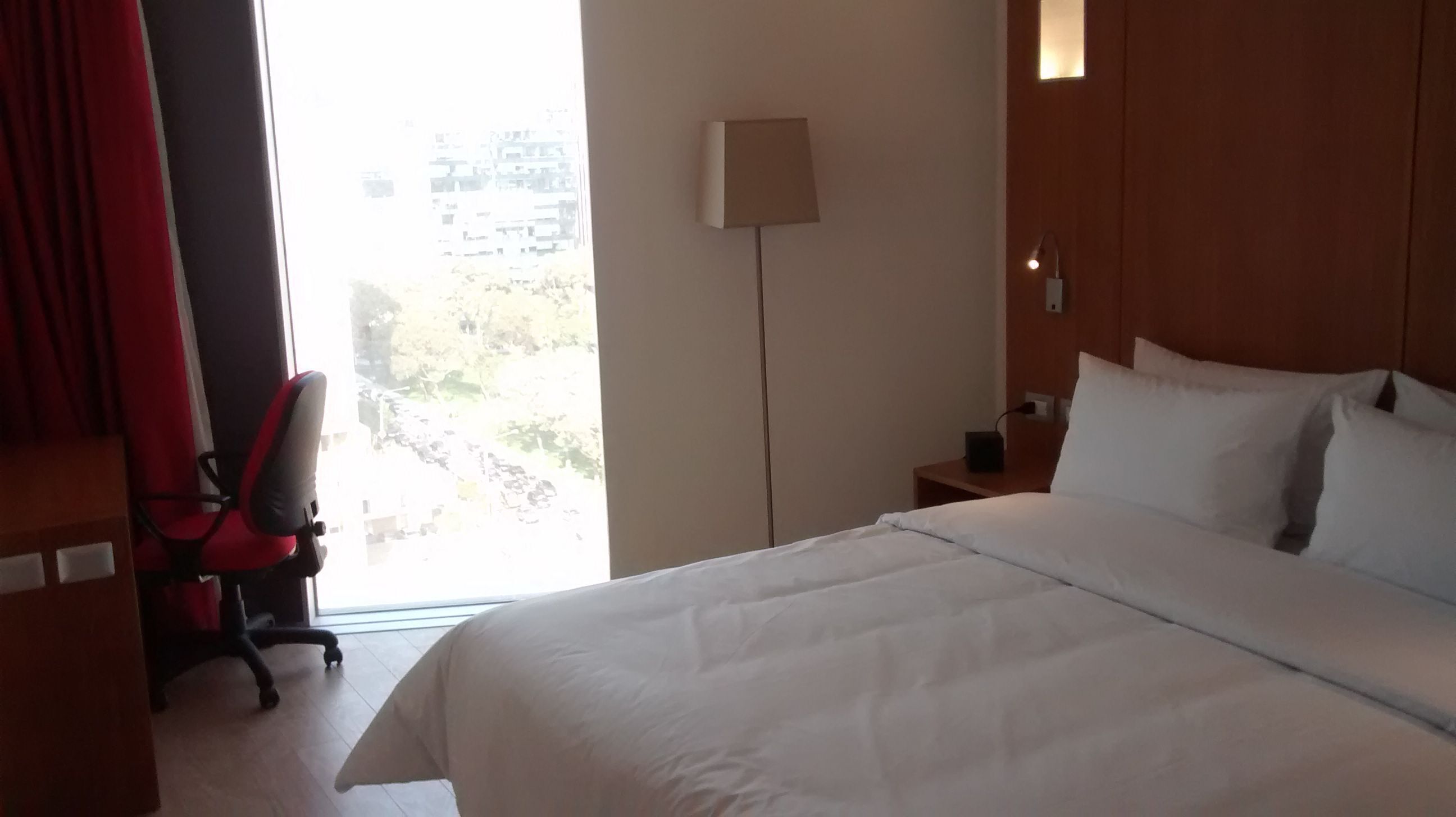 Una habitación de hotel con una cama grande, un escritorio con lámpara y una silla.