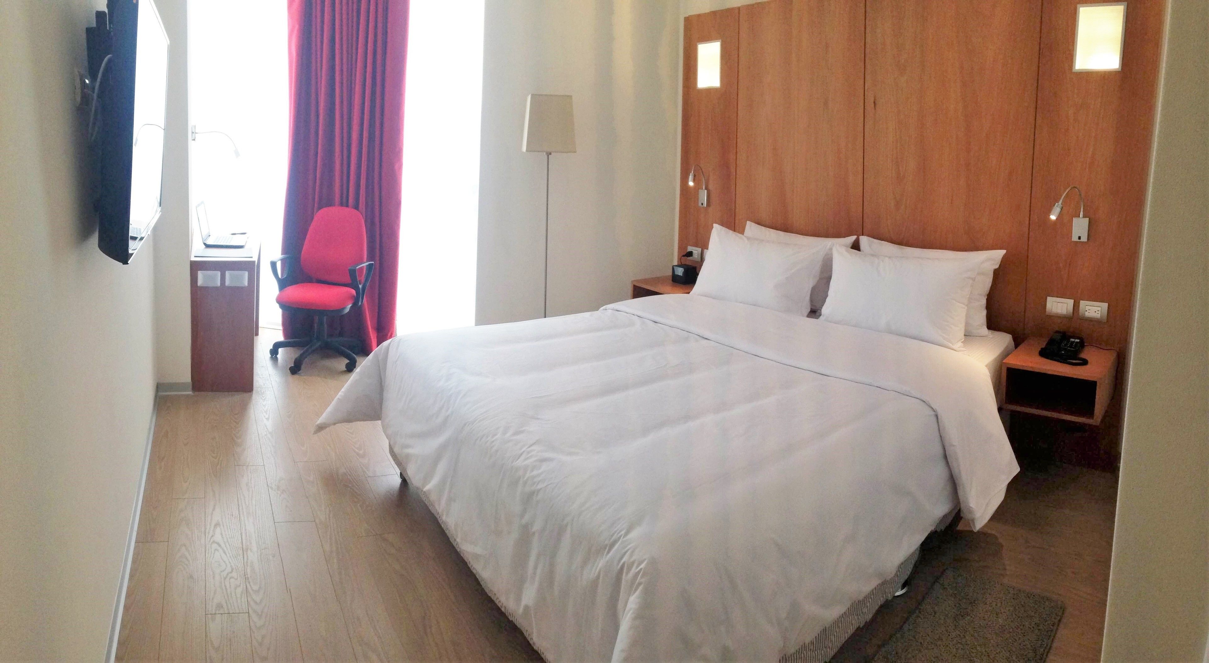 Una habitación de hotel con una cama grande, un escritorio con una silla, una lámpara y un teléfono en una mesita de noche.