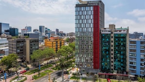 Un moderno rascacielos con una llamativa banda vertical roja, rodeado de otros edificios y áreas verdes.