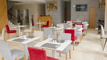 A modern restaurant with white and red tables, grey chairs, and a wine display on the wall.