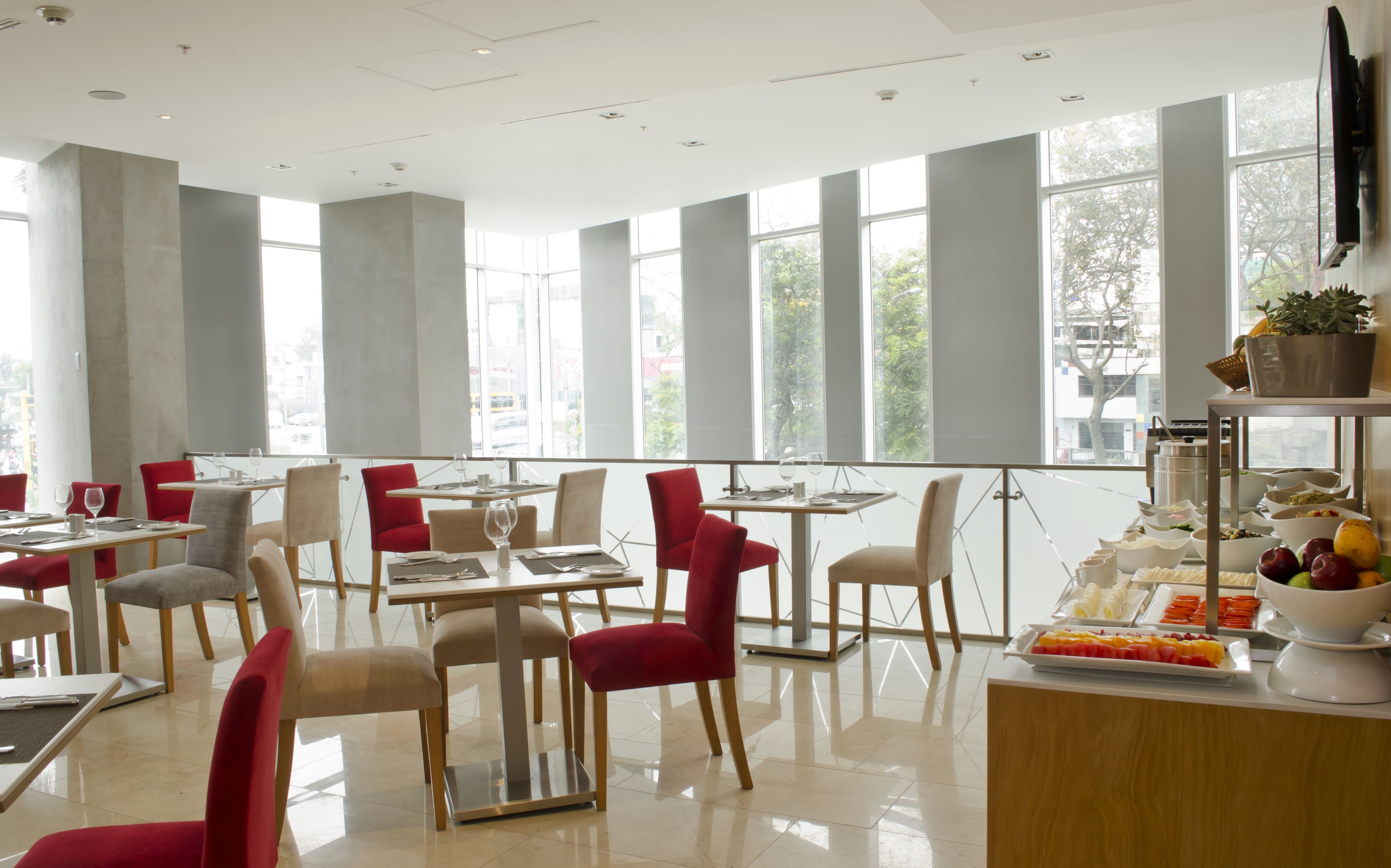 A modern restaurant with high ceilings, large windows, and a variety of seating options including red and beige chairs.