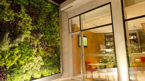 Un edificio moderno con una amplia entrada de vidrio, un jardín vertical verde y un interior visible con asientos y mesas.