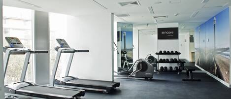 Uma academia com esteiras, bicicleta ergométrica e um banco de musculação.