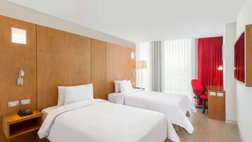 Habitación de hotel con dos camas, un escritorio, una silla y un ventanal con cortinas.