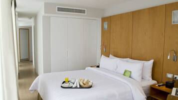A hotel room with a bed, a wooden wardrobe, a bedside table with a phone, and a tray with breakfast items.