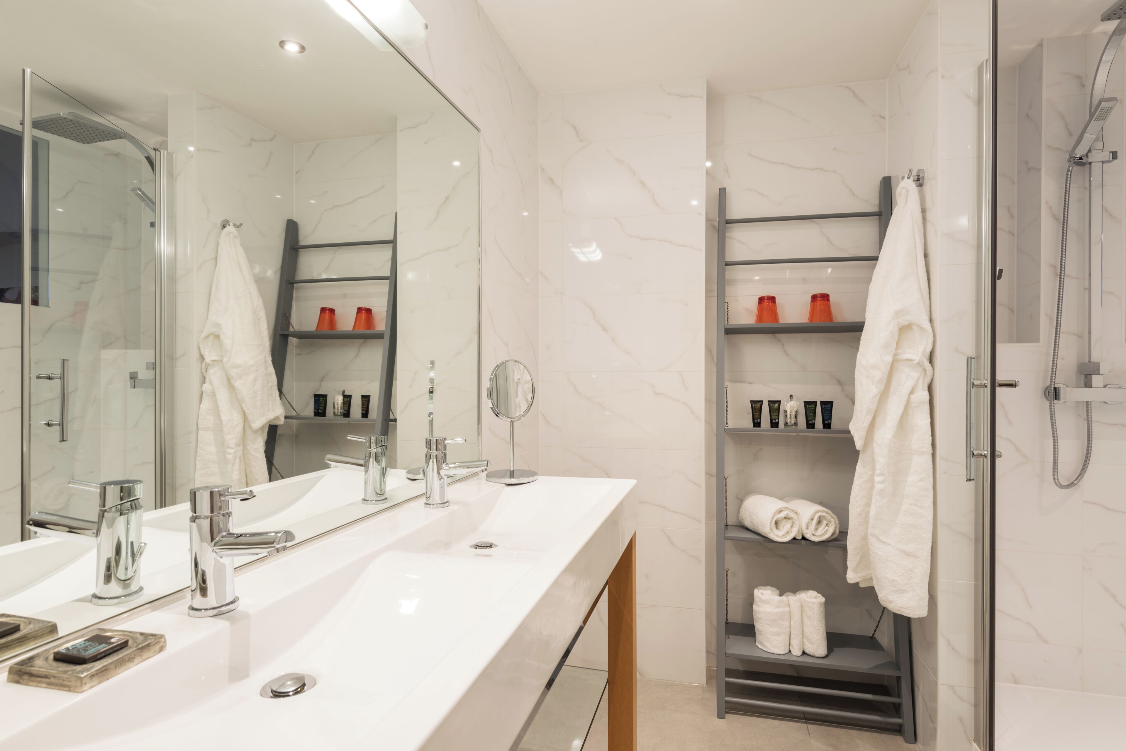A modern bathroom with two sinks, a large mirror, and a shower area.
