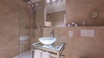 Ein modernes Badezimmer mit einer gläsernen Duschkabine, einem Waschbecken aus Glas und einem Spiegel darüber.