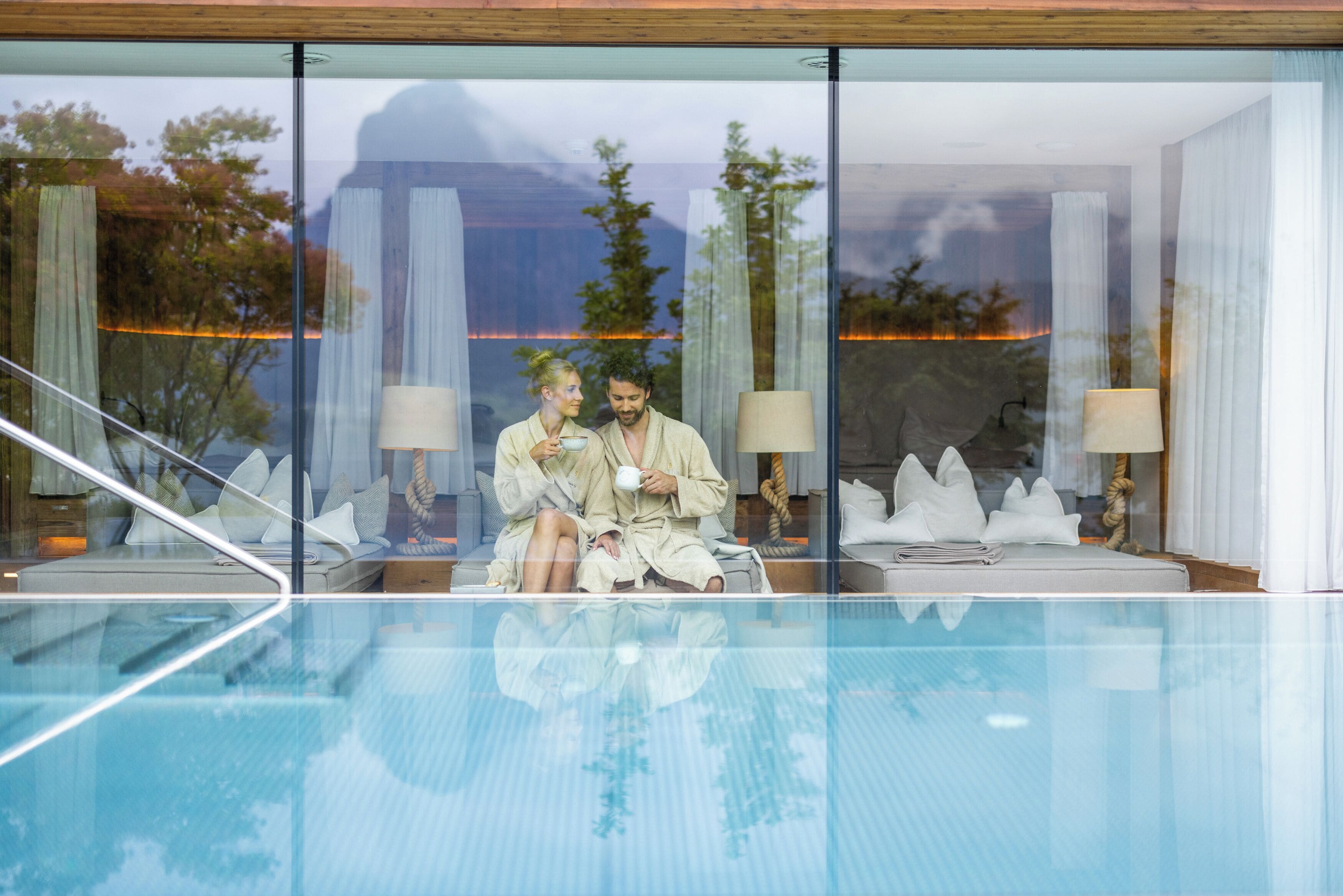 A couple sitting by a poolside with a view of a mountain and trees.