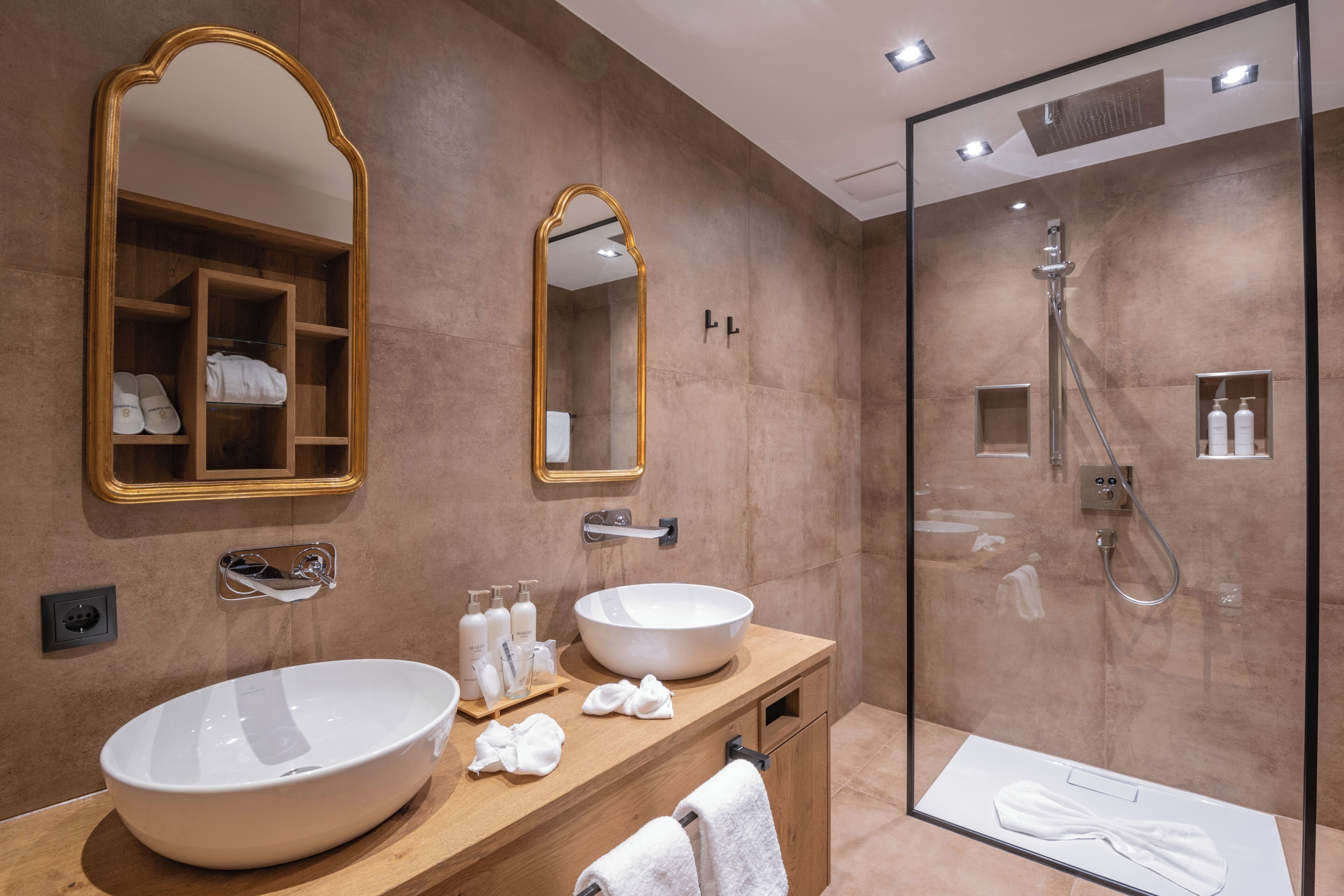 Un baño moderno con un lavamanos ovalado grande, dos espejos, una ducha con mampara de vidrio y un mueble de tocador de madera.