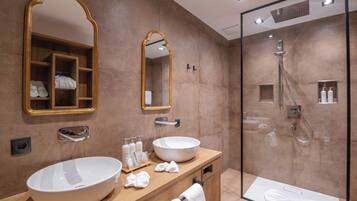 Un baño moderno con un lavamanos ovalado grande, dos espejos, una ducha con mampara de vidrio y un mueble de tocador de madera.