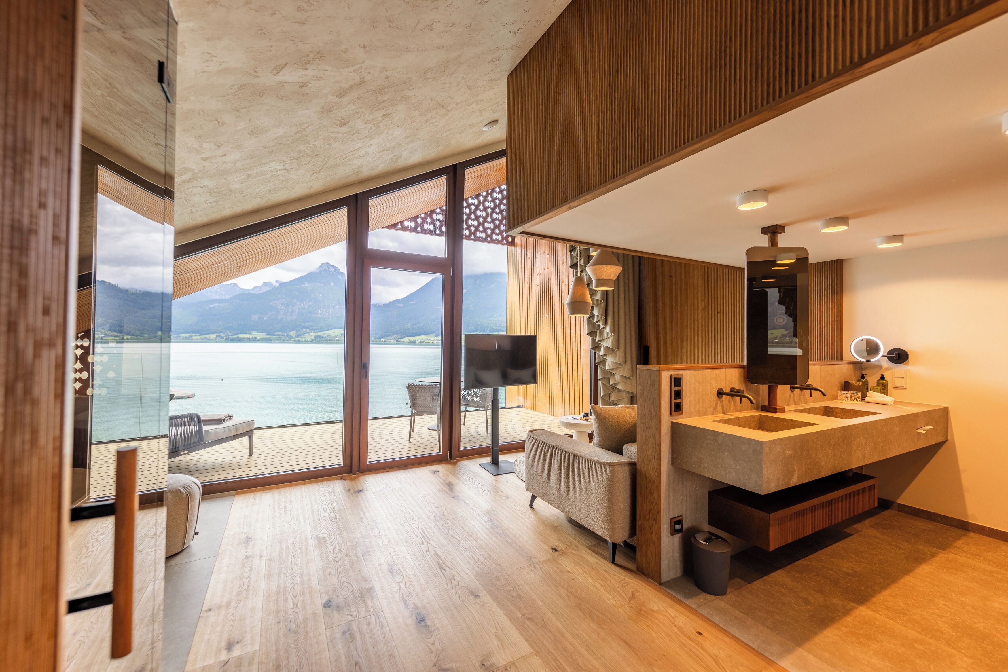 A modern bathroom with a large mirror, dual sinks, and a view of a lake and mountains.