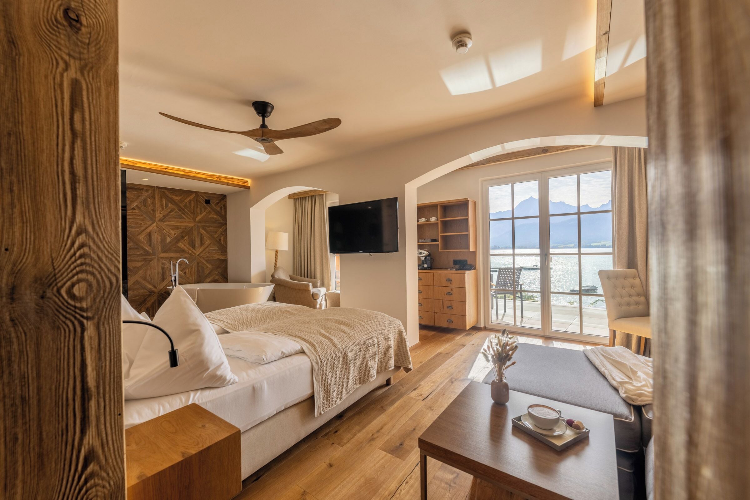 A hotel room with a bed, a desk, a TV, and a balcony with a view.