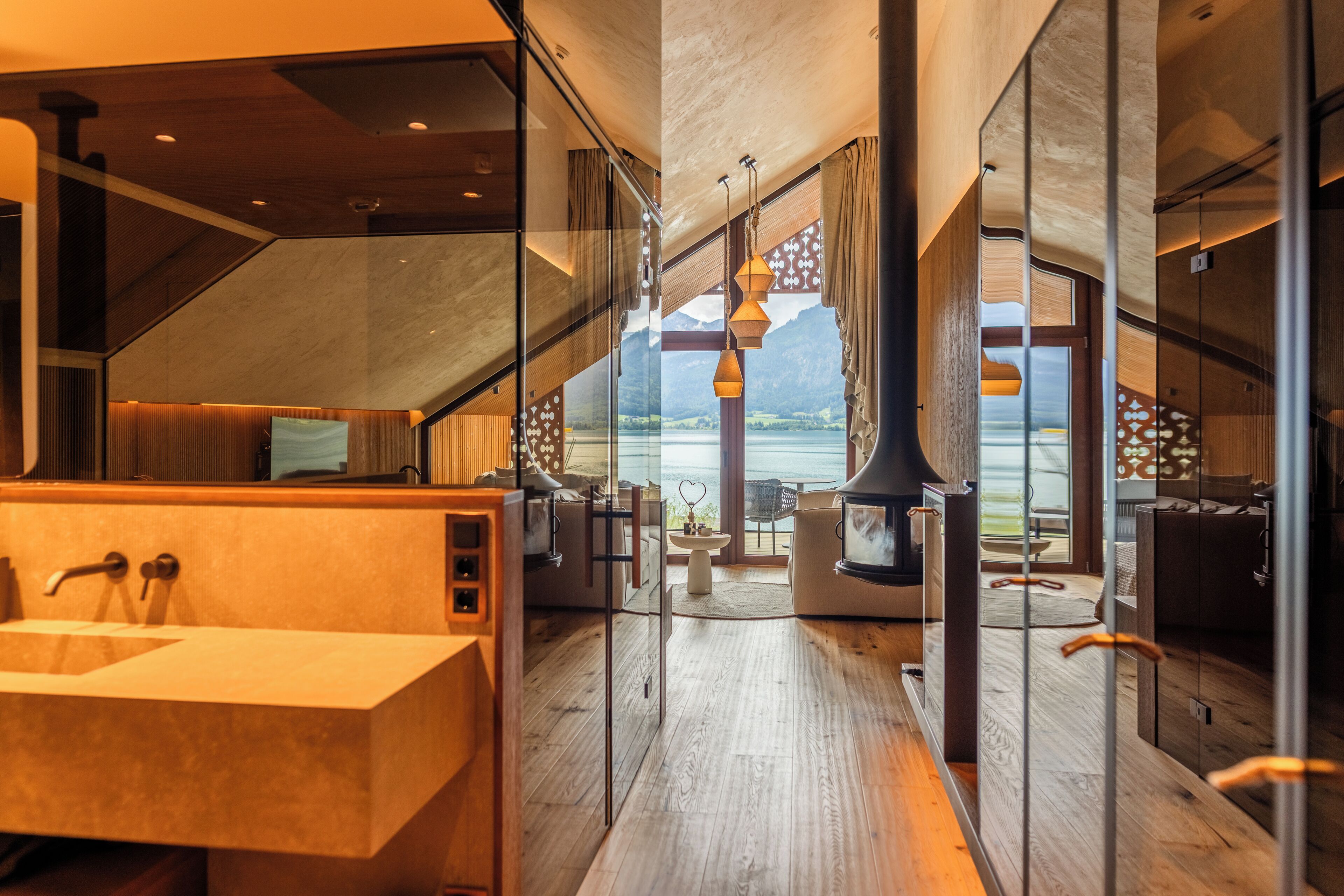 A modern bathroom with a large sink, wooden flooring, and a view of a lake through large windows.