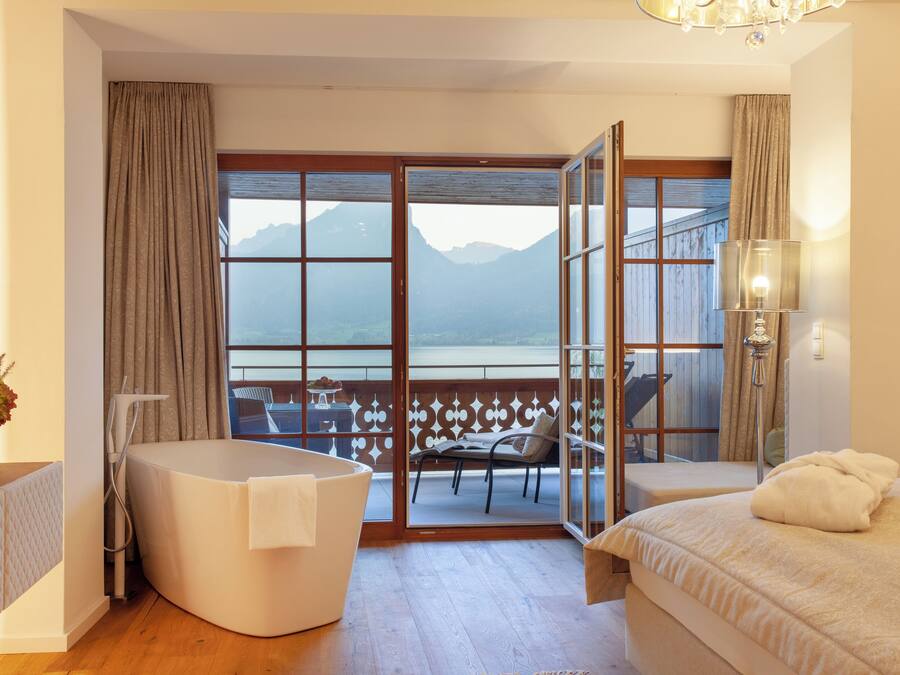 Quarto com cama grande, banheira e vista para montanhas através de uma porta de correr de vidro.