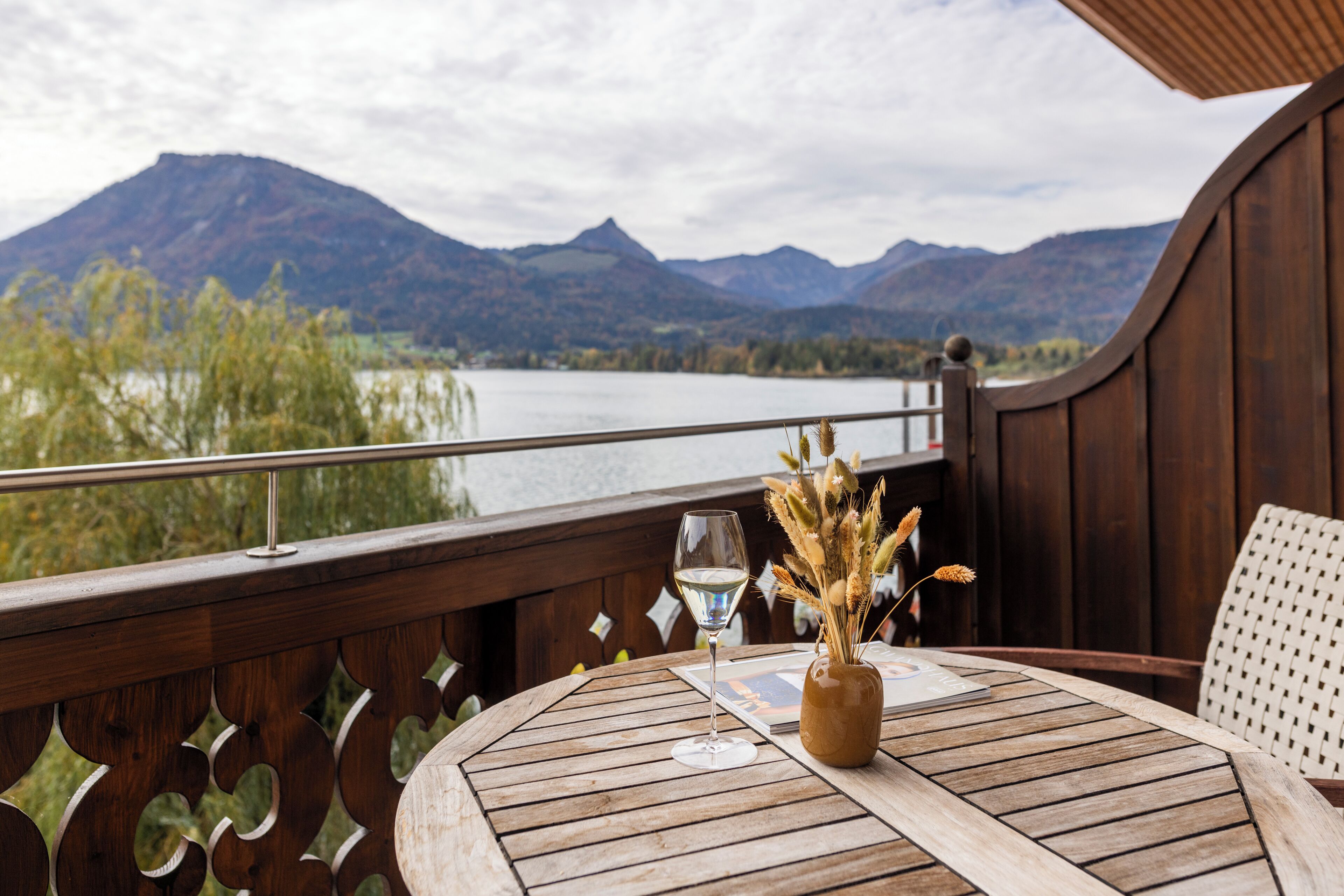 Una terraza de madera con una mesa y sillas, con vista a un lago y montañas.
