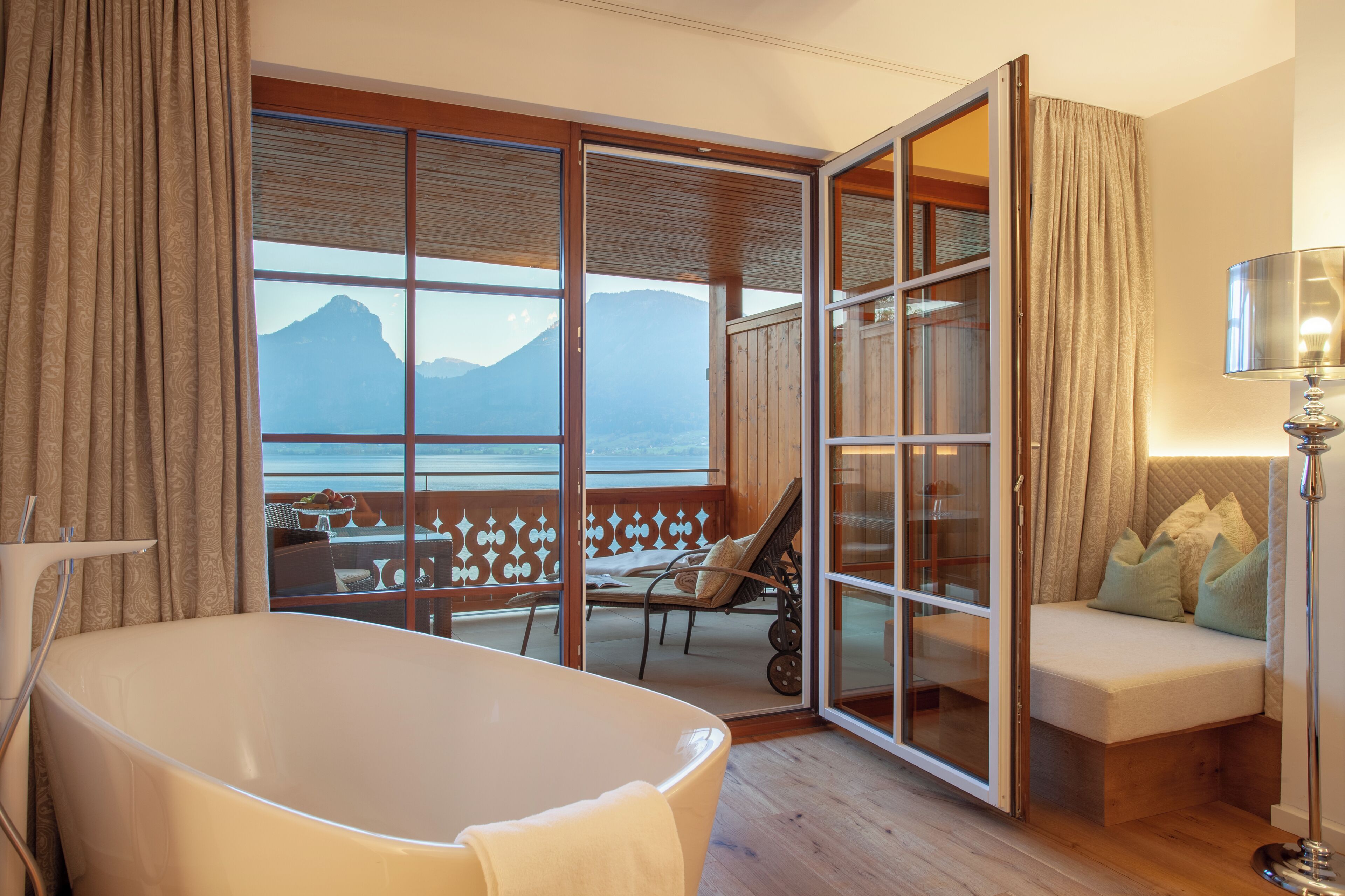 A room with a bathtub, a sofa, and a view of mountains through large windows.