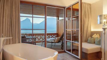 A room with a bathtub, a sofa, and a view of mountains through large windows.