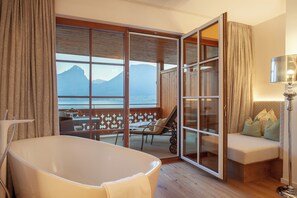 A room with a bathtub, a sofa, and a view of mountains through large windows.