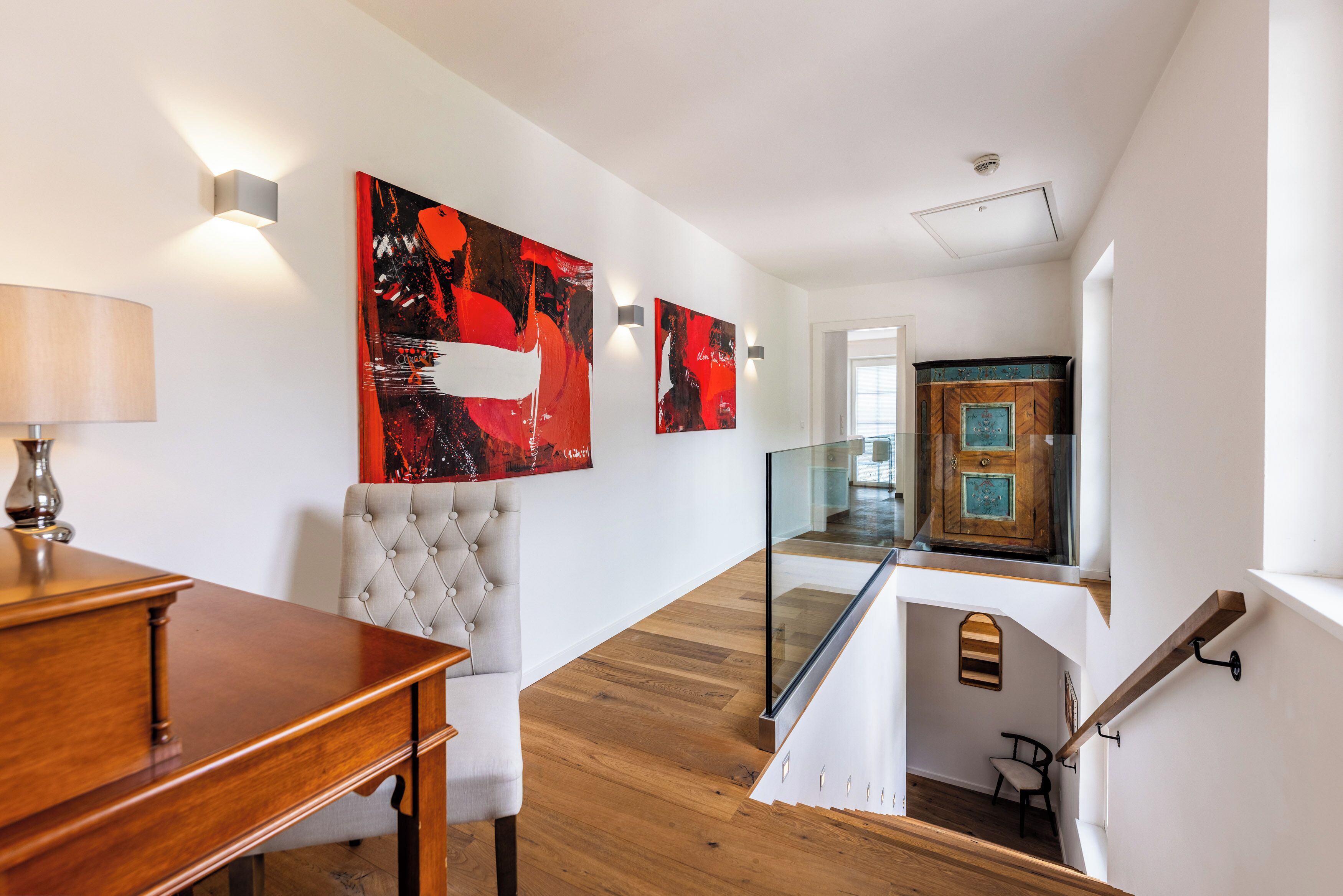 A modern interior with a staircase, wooden flooring, a dining area with a table and chairs, and artwork on the walls.