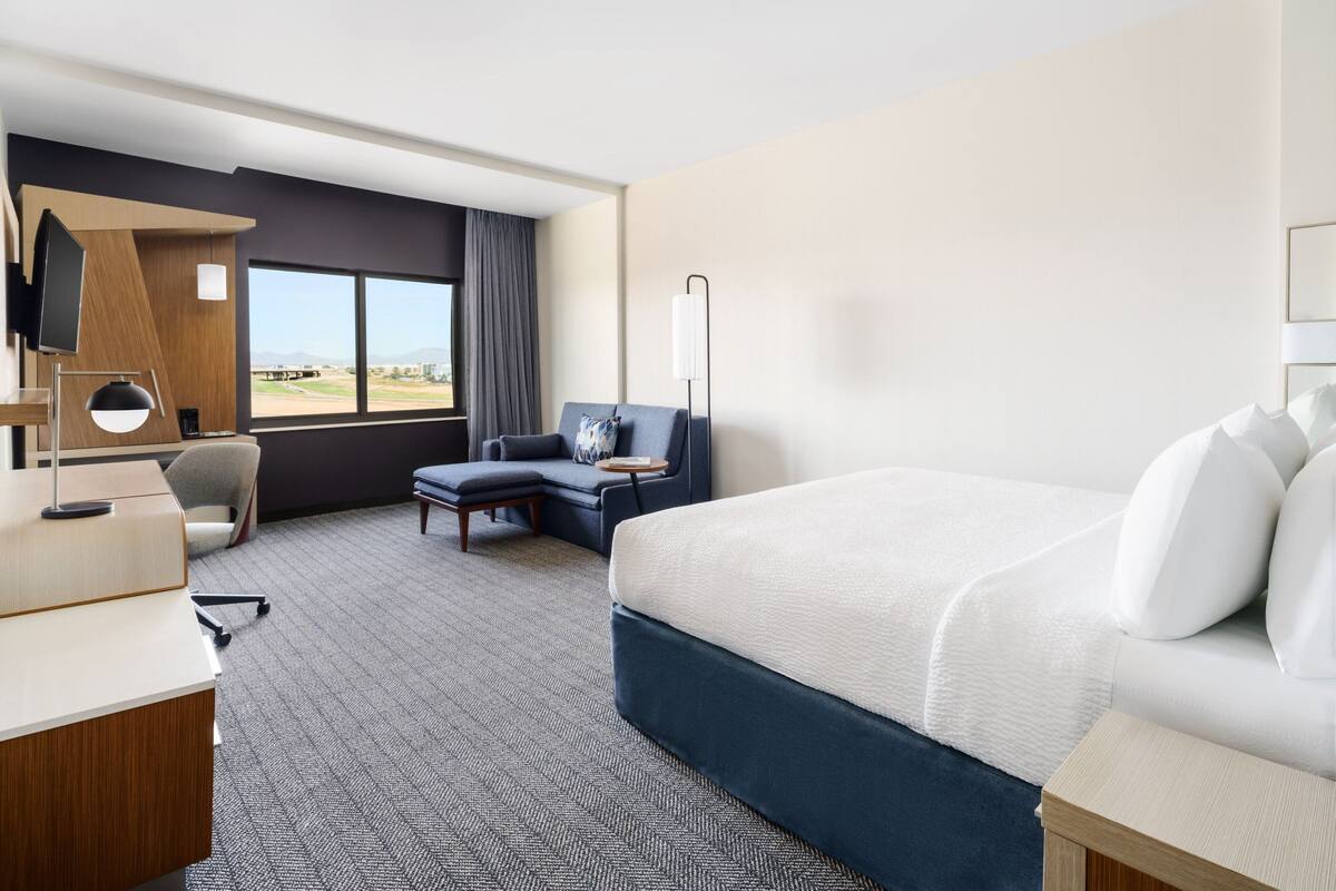 Quarto de hotel com uma cama grande, uma escrivaninha, uma cadeira e vista para o exterior.