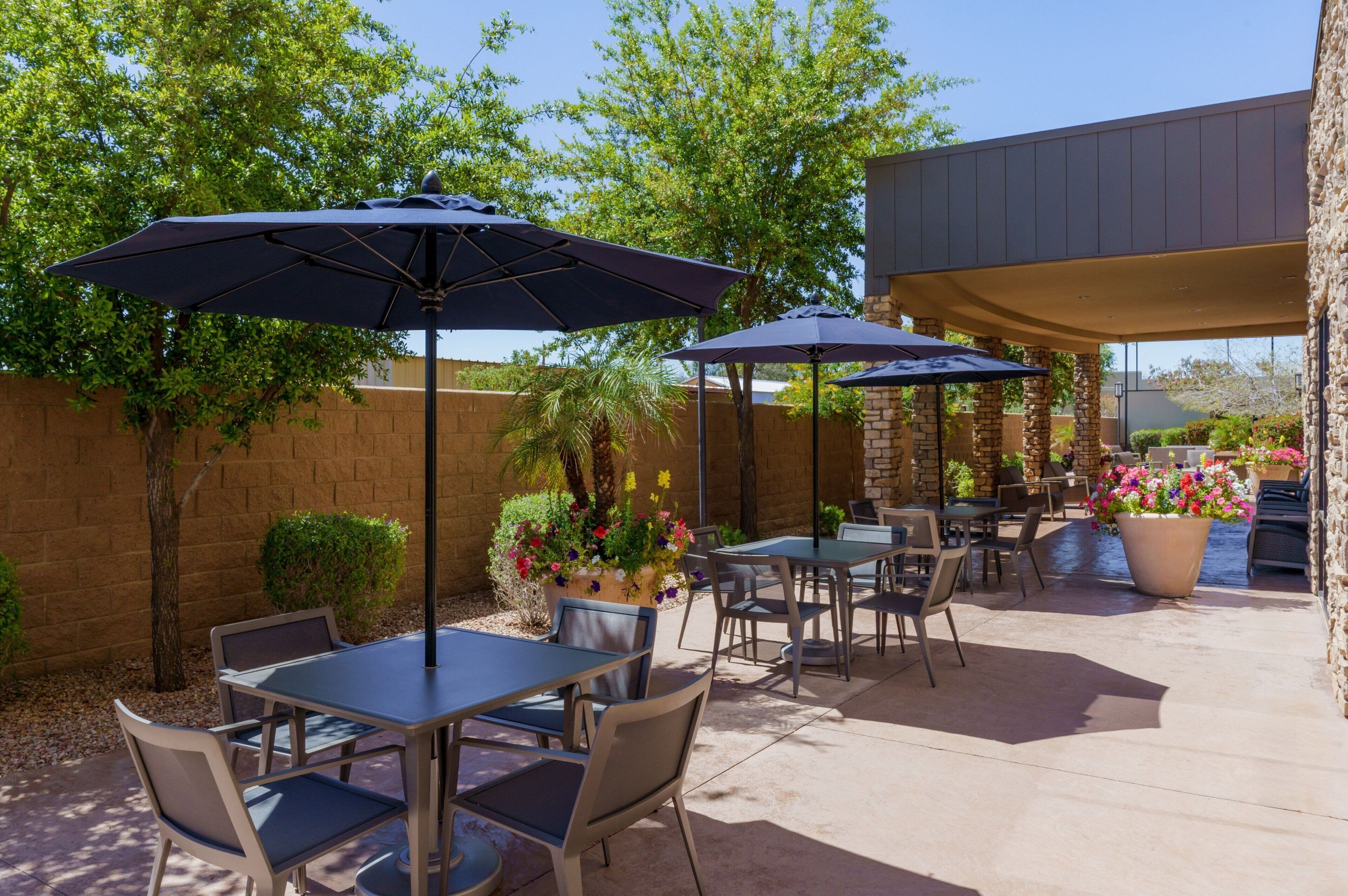 Un espace extérieur aménagé en terrasse, avec des tables, des chaises, des parasols et des plantes en pot.
