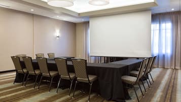 Ein Konferenzraum mit langem Tisch, Stühlen, einer Projektionsleinwand und Teppichboden.