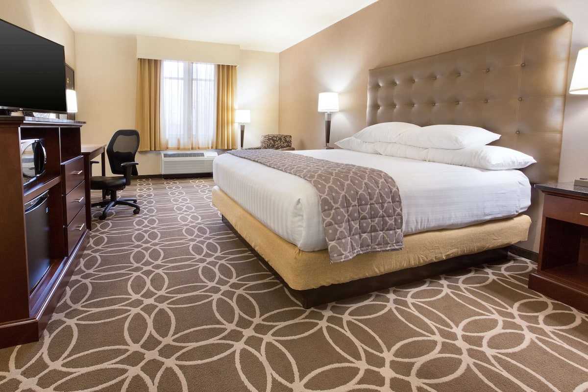 A hotel room with a large bed, a desk with a television, a chair, and a desk lamp.