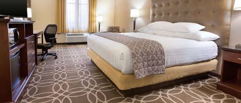A hotel room with a large bed, a desk with a television, a chair, and a desk lamp.
