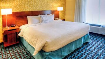 A hotel room with a large bed, two bedside lamps, a telephone, and an air conditioning unit.