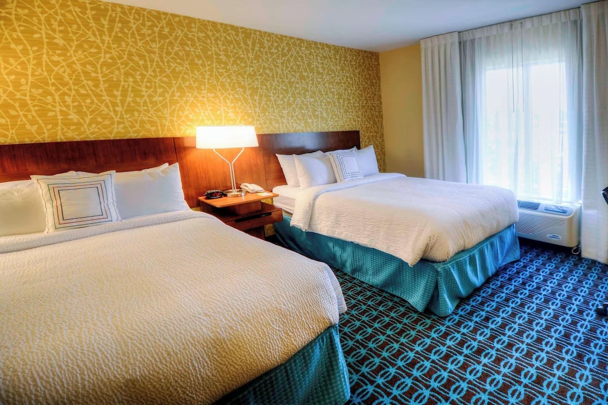 Une chambre d’hôtel avec deux lits, une tête de lit en bois, une table de chevet avec une lampe et une fenêtre avec des rideaux.