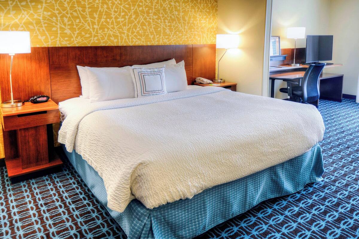 Une chambre d’hôtel avec un grand lit, deux tables de chevet avec des lampes, un bureau avec une chaise et un téléviseur.