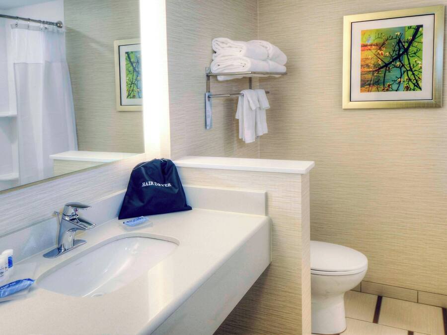 A bathroom with a white sink, a mirror, a towel rack with folded towels, a toilet, and a framed picture on the wall.