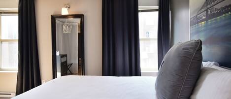 Habitación de hotel con una cama grande, cortinas oscuras, un espejo y un cuadro de un paisaje urbano en la pared.