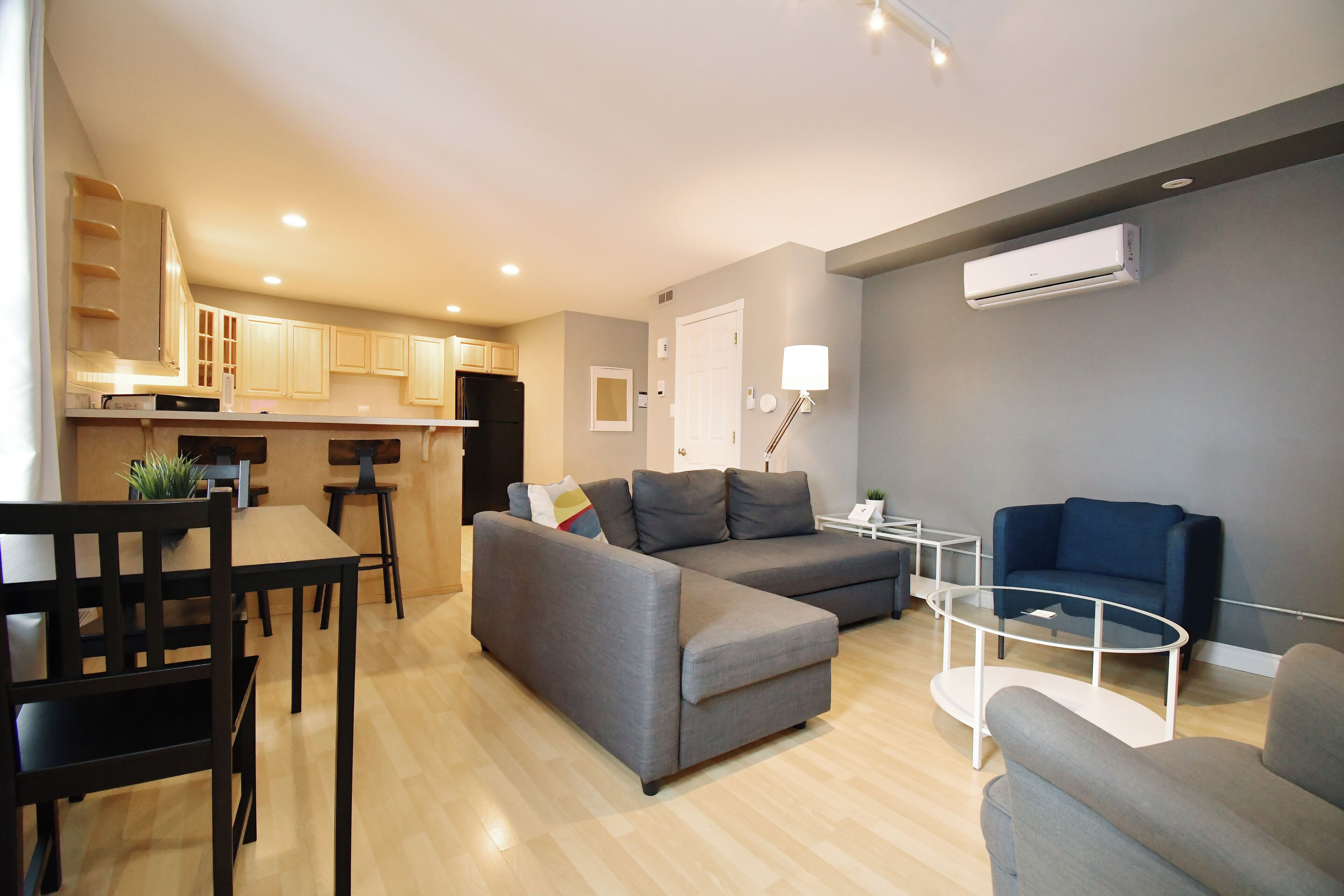A modern living room with a grey sofa, a dining table with chairs, a small coffee table, and a blue armchair.